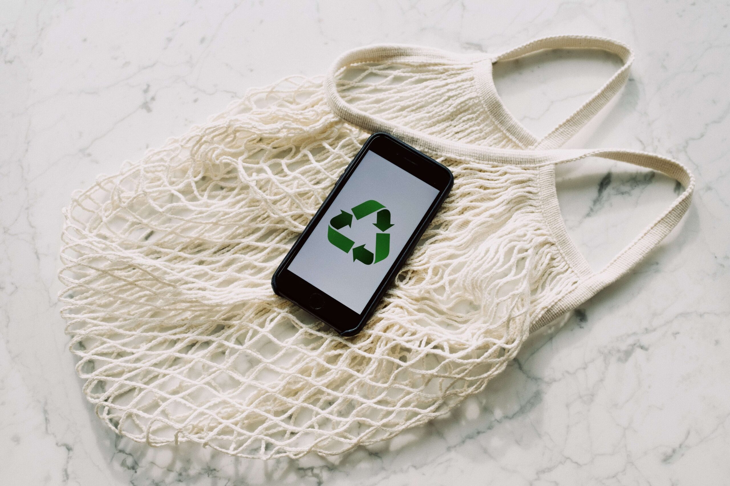 A phone showing reduce-reuse-recycle symbol placed on a clothe shopping bag. White background